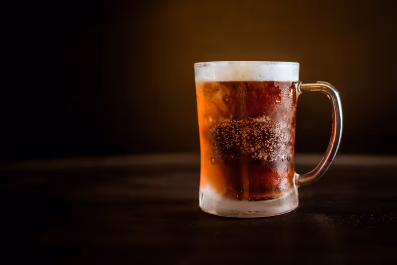 A cold mug of dark beer with a thick head sitting on the bar at the end of the night