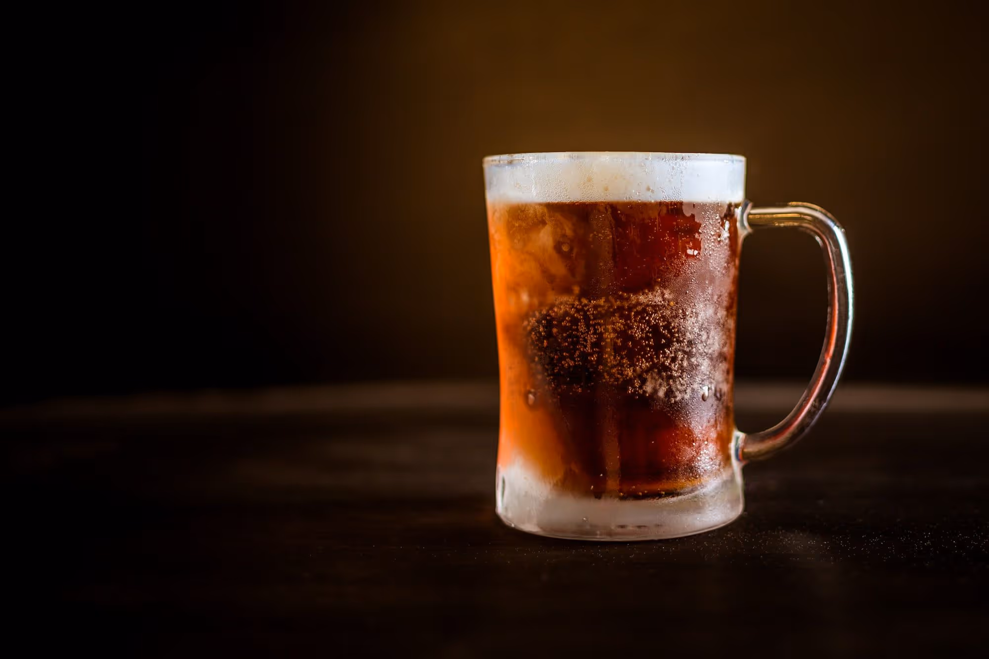 A cold mug of dark beer with a thick head sitting on the bar at the end of the night
