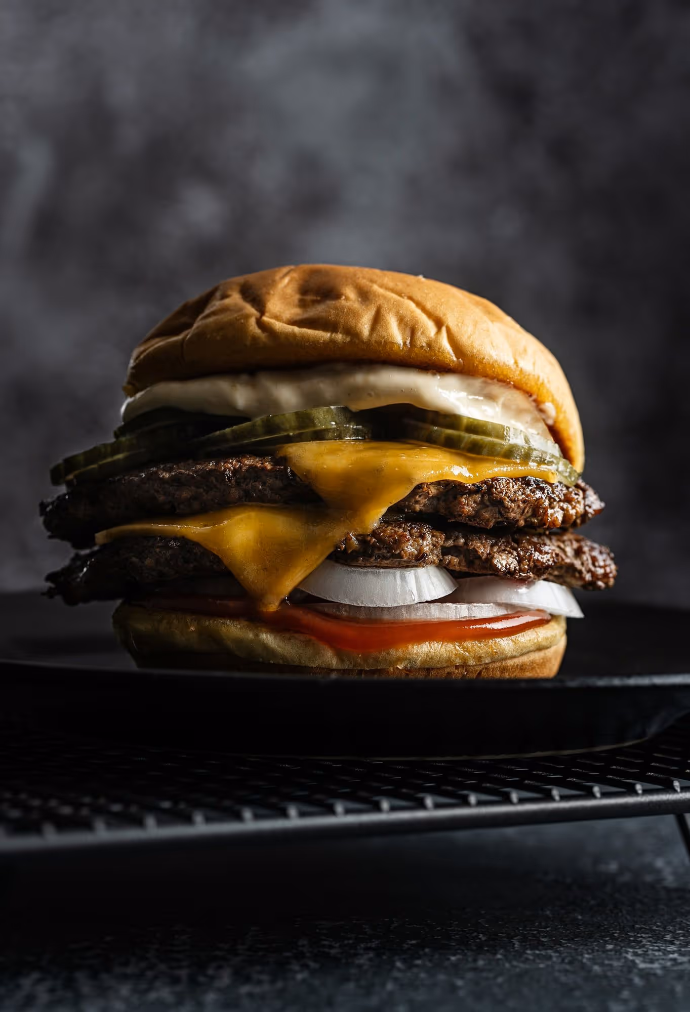 A double cheeseburger stacked with pickles and raw white onion on a black plate