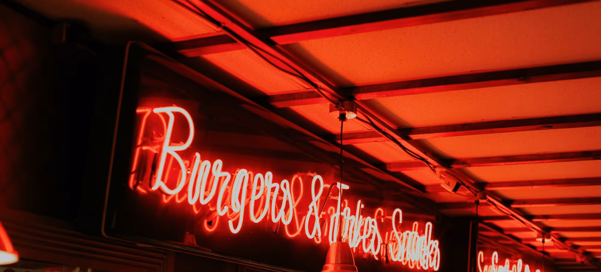 Red neon script reading Burgers and Fries burning under the low ceiling over the order counter
