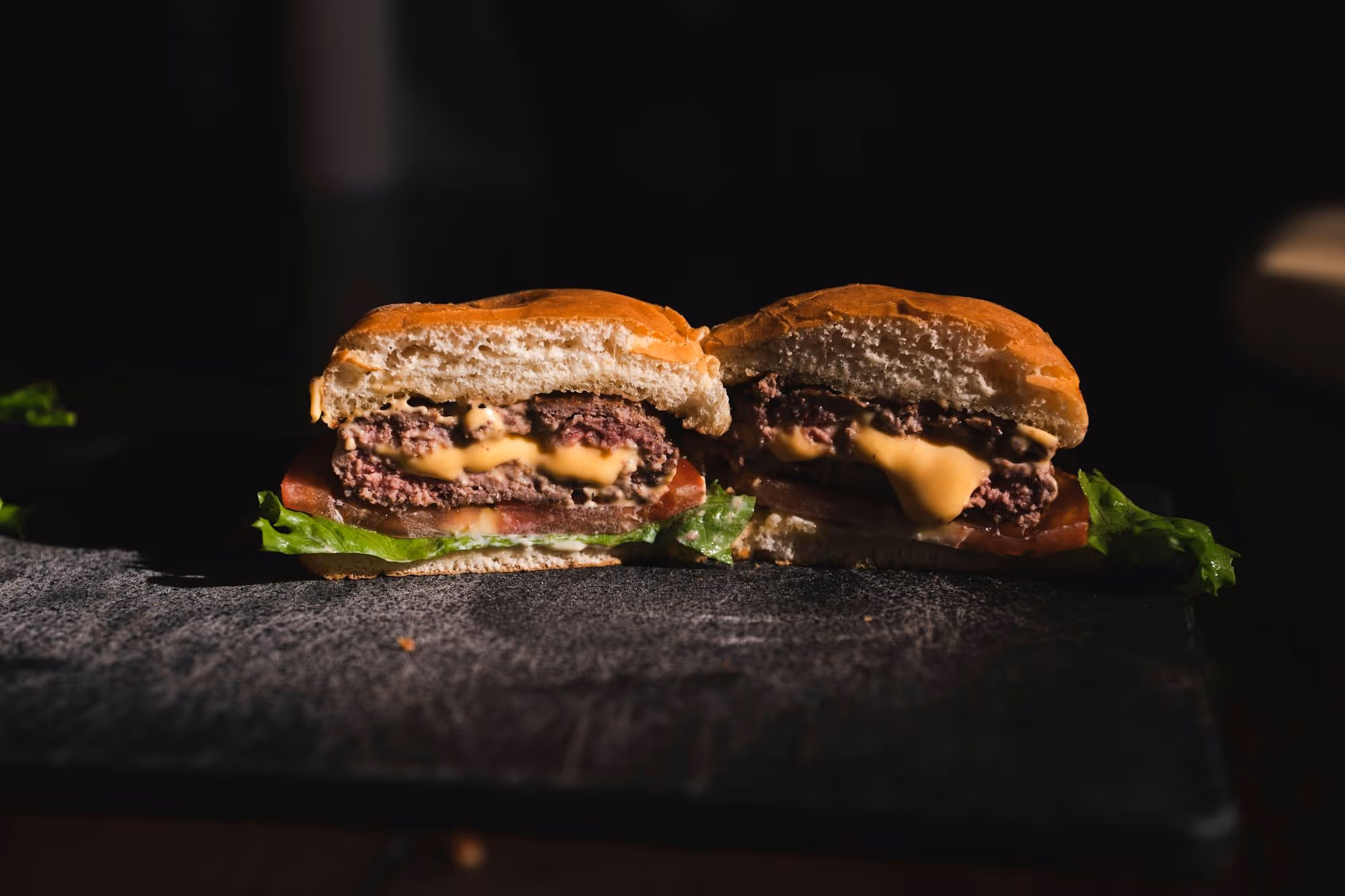 A double cut in half on a charred board, showing the two thin patties and the lace crust